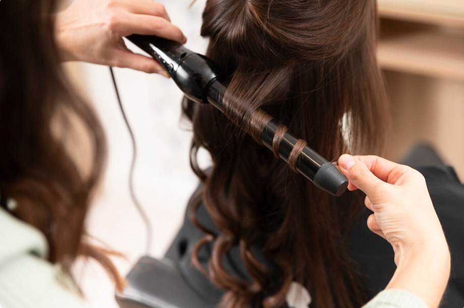 Hairdresser curling a client's long brown hair with a curling iron at a salon