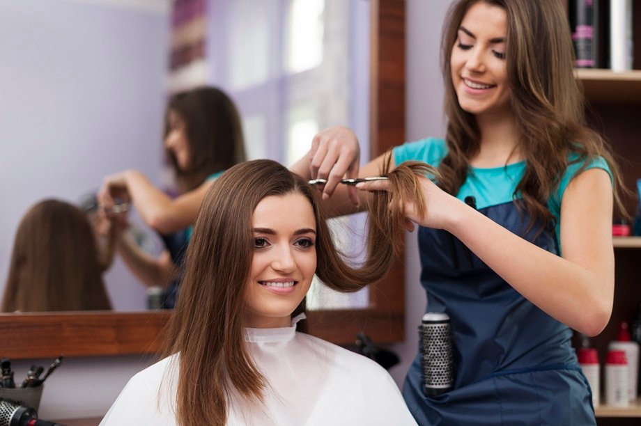 Hairdresser trims and styles a client's brown hair in a salon, both smiling