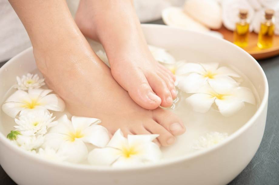 Feet soaking in a white bowl of water with floating white plumeria flowers, a spa pedicure scene, relaxing and refreshing